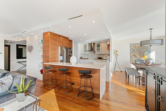 kitchen featuring wall chimney range hood, light hardwood / wood-style flooring, white cabinets, a kitchen bar, and stainless steel fridge with ice dispenser