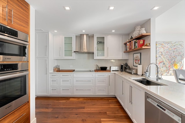 kitchen featuring appliances with stainless steel finishes, dark hardwood / wood-style floors, sink, white cabinets, and wall chimney range hood