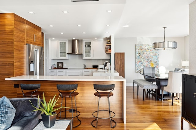 kitchen featuring white cabinetry, a breakfast bar, stainless steel fridge, and wall chimney exhaust hood