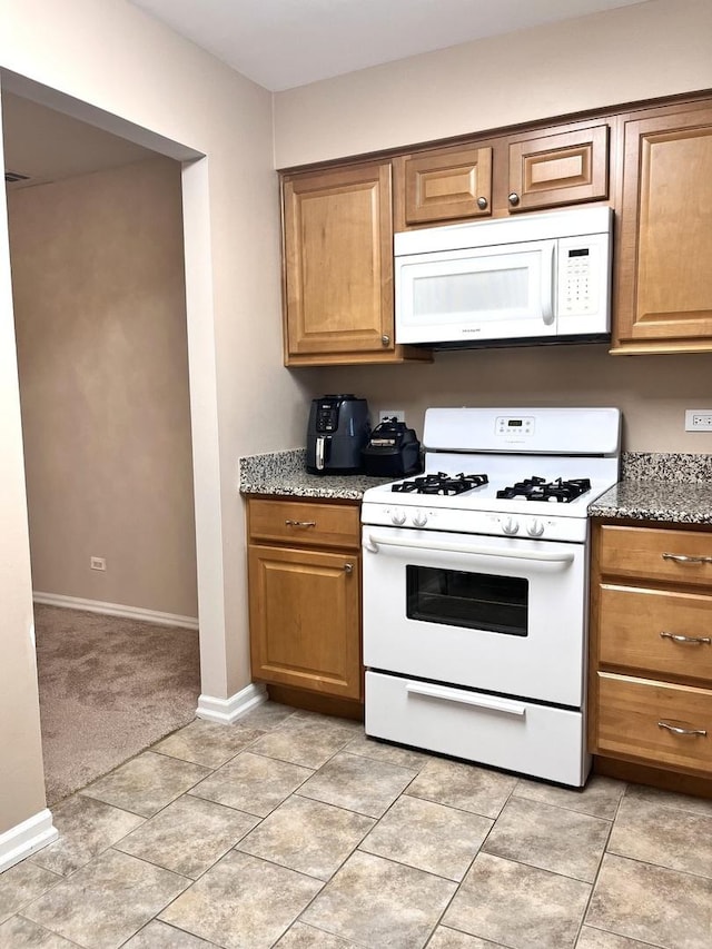 kitchen with dark stone countertops, white appliances, and light tile patterned flooring