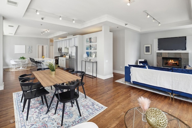 dining area featuring a tiled fireplace, dark wood-type flooring, and a raised ceiling