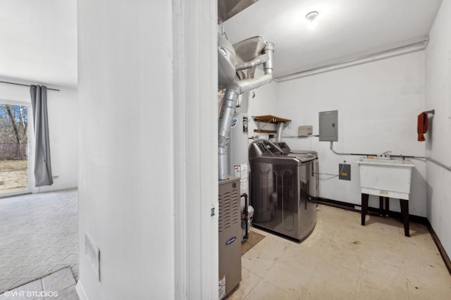 washroom featuring washing machine and clothes dryer, electric panel, sink, and gas water heater