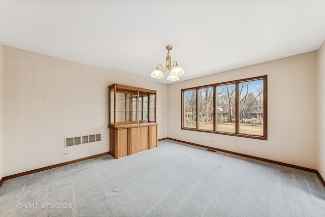 carpeted spare room with visible vents, baseboards, and an inviting chandelier