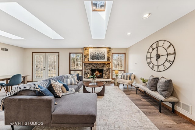 living area with a skylight, visible vents, a stone fireplace, and wood finished floors