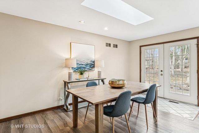 dining room featuring light wood-style floors, a skylight, french doors, and a healthy amount of sunlight