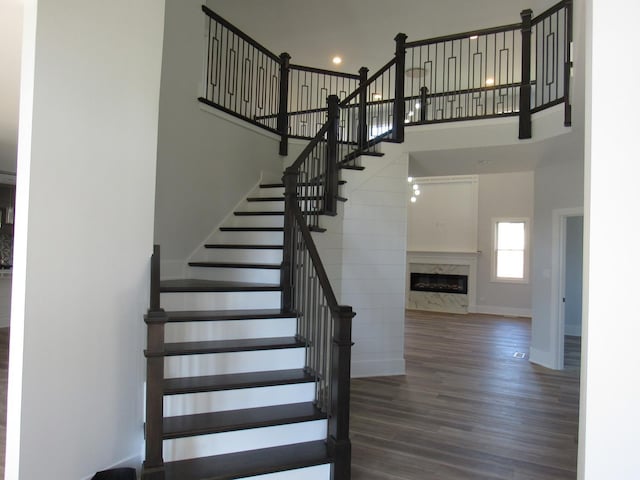 stairs with a towering ceiling, a premium fireplace, and hardwood / wood-style floors