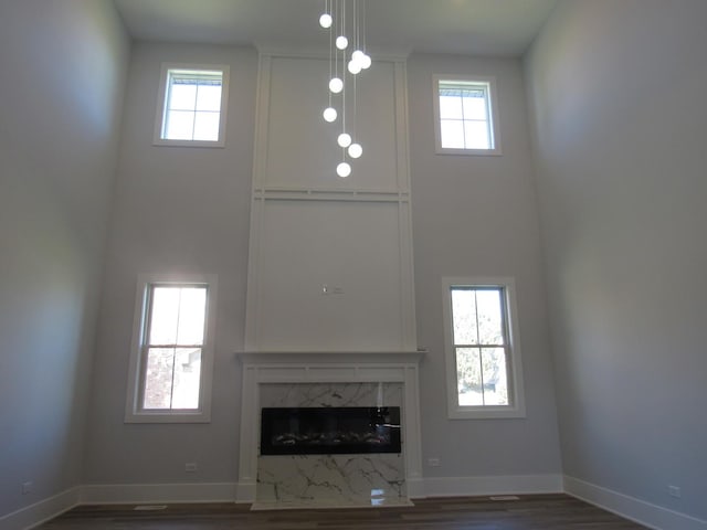 unfurnished living room with a high end fireplace, dark hardwood / wood-style flooring, a high ceiling, and plenty of natural light