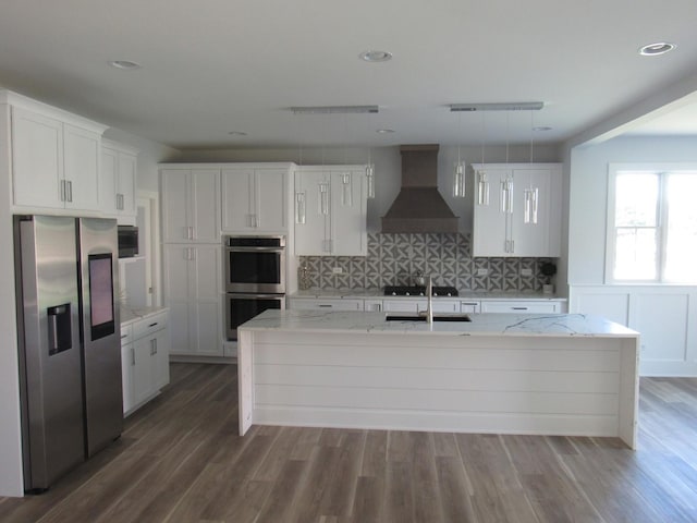 kitchen with appliances with stainless steel finishes, decorative light fixtures, a kitchen island with sink, and custom exhaust hood