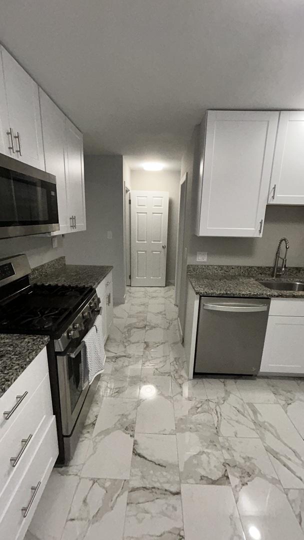 kitchen with appliances with stainless steel finishes, sink, dark stone counters, and white cabinets