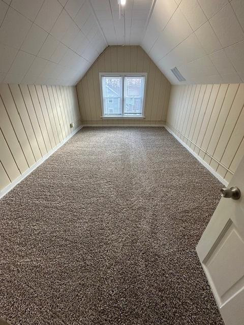 additional living space with lofted ceiling, carpet floors, and wooden walls