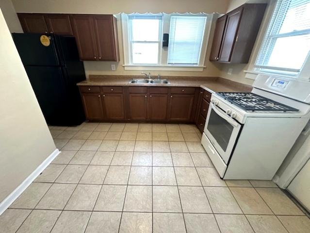 kitchen with black refrigerator, sink, gas range gas stove, and light tile patterned floors