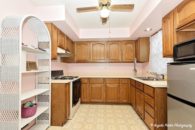 kitchen with sink, gas range, a tray ceiling, stainless steel fridge, and ceiling fan