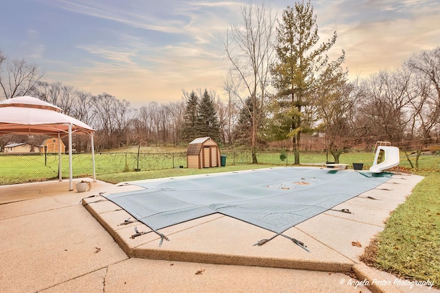 pool at dusk featuring a storage shed, a lawn, a water slide, a gazebo, and a patio area