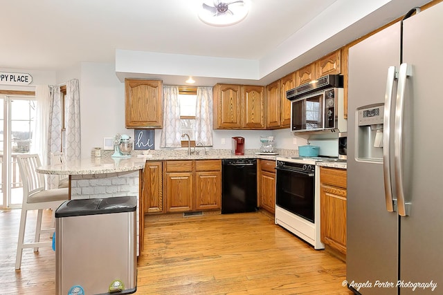 kitchen with sink, light wood-type flooring, plenty of natural light, kitchen peninsula, and black appliances