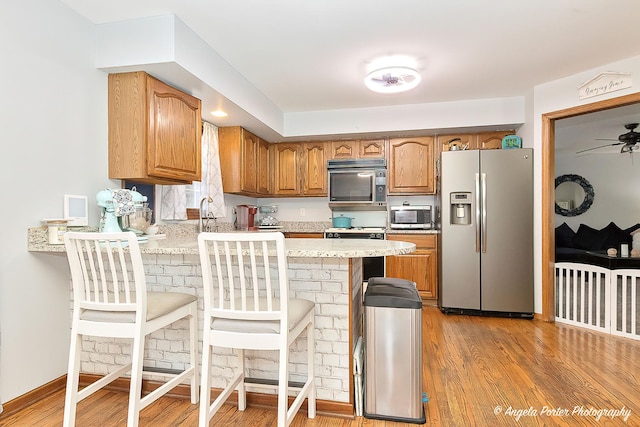 kitchen with light wood-type flooring, a kitchen breakfast bar, kitchen peninsula, ceiling fan, and stainless steel appliances