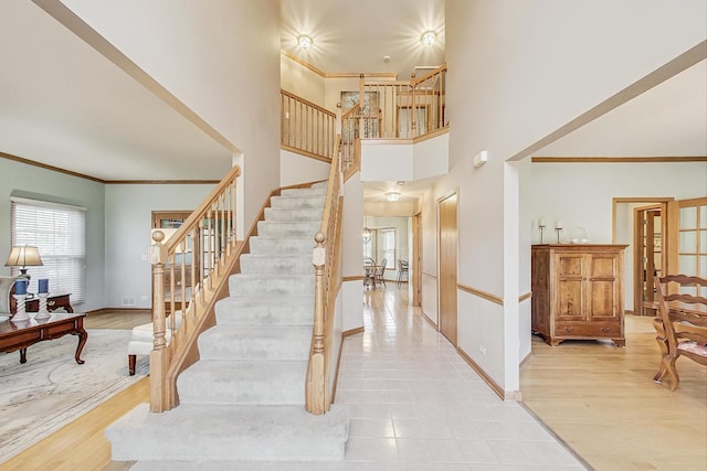 stairway with crown molding, wood-type flooring, and a towering ceiling