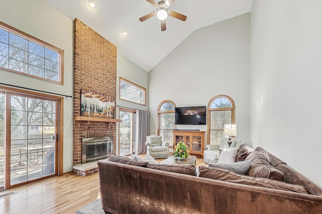 living room featuring ceiling fan, high vaulted ceiling, a fireplace, and light hardwood / wood-style flooring