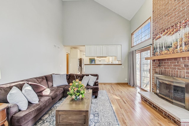 living room with a brick fireplace, light hardwood / wood-style flooring, and high vaulted ceiling