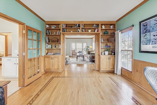 interior space with ornamental molding, wooden walls, and light wood-type flooring