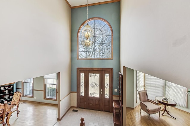 foyer with crown molding, a notable chandelier, a towering ceiling, and light hardwood / wood-style floors