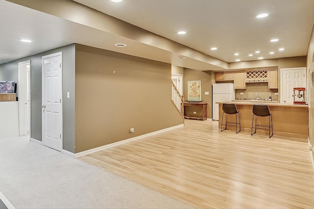 kitchen featuring sink, light hardwood / wood-style flooring, a breakfast bar area, white fridge, and light brown cabinets