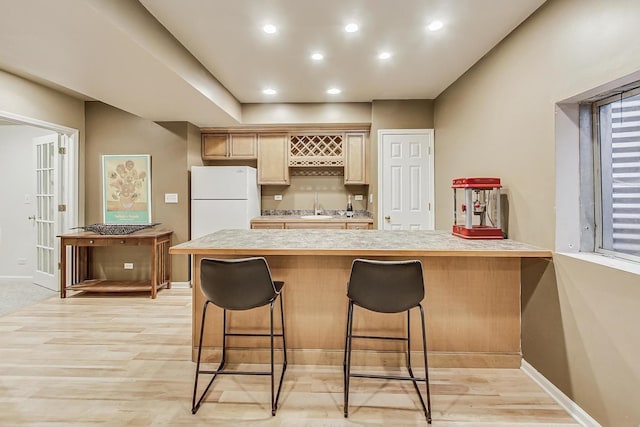 kitchen with light brown cabinetry, sink, a kitchen breakfast bar, white fridge, and light hardwood / wood-style flooring