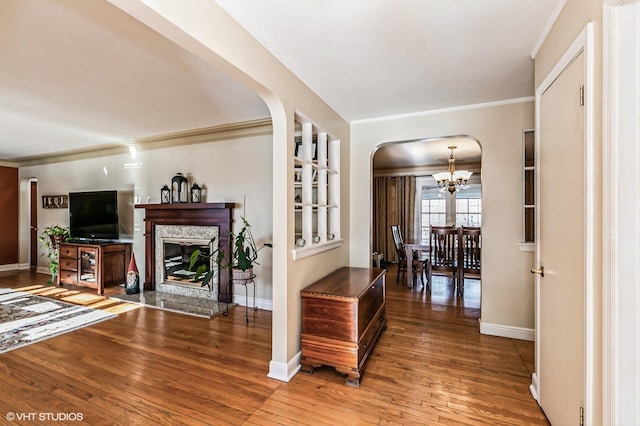 interior space with arched walkways, a notable chandelier, a fireplace, wood finished floors, and baseboards