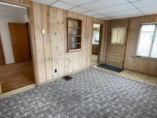 carpeted spare room with a drop ceiling and wooden walls