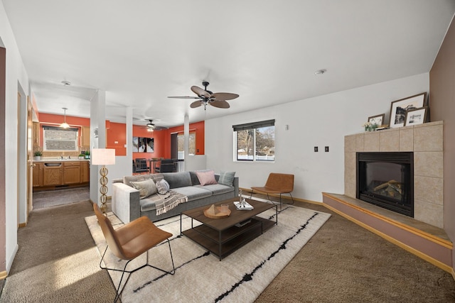 living room with a tile fireplace, sink, ceiling fan, and dark carpet