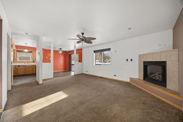 unfurnished living room featuring ceiling fan, sink, dark carpet, and a tile fireplace