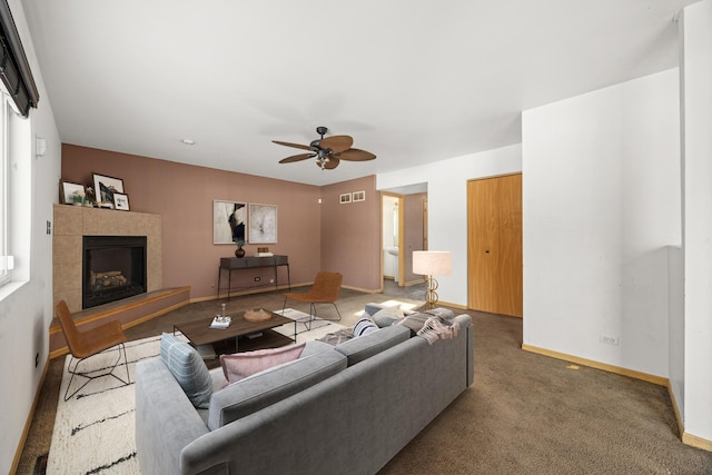 living room with ceiling fan, a tiled fireplace, and carpet