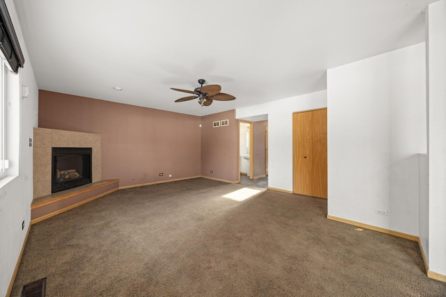 unfurnished living room featuring a tiled fireplace, ceiling fan, and dark carpet