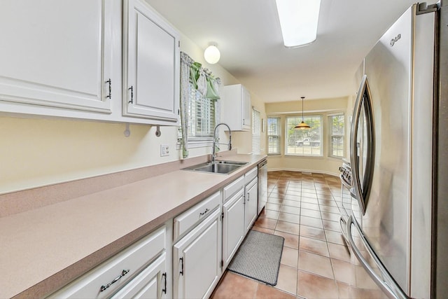 kitchen with sink, hanging light fixtures, light tile patterned floors, appliances with stainless steel finishes, and white cabinets