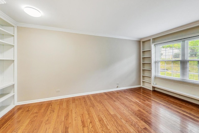 empty room with crown molding, built in features, and light wood-type flooring