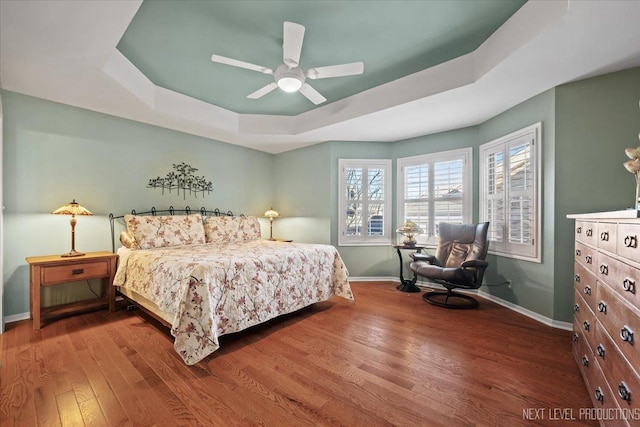 bedroom with hardwood / wood-style flooring, a raised ceiling, and ceiling fan