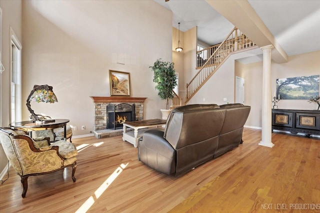 living room featuring a stone fireplace, a towering ceiling, a healthy amount of sunlight, and light wood-type flooring