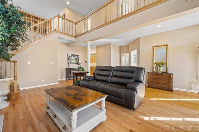 living room featuring ornate columns, a towering ceiling, and light hardwood / wood-style floors