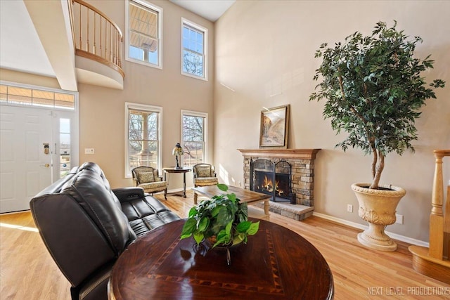 living room featuring a stone fireplace, light hardwood / wood-style floors, and a towering ceiling