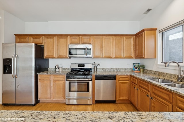 kitchen featuring appliances with stainless steel finishes, sink, light stone counters, and light wood-type flooring