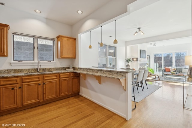 kitchen featuring a kitchen bar, sink, decorative light fixtures, light hardwood / wood-style flooring, and kitchen peninsula