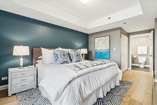 bedroom featuring light hardwood / wood-style flooring, ensuite bath, and a tray ceiling