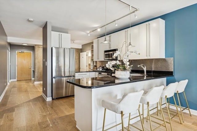 kitchen with hanging light fixtures, stainless steel appliances, kitchen peninsula, and white cabinets