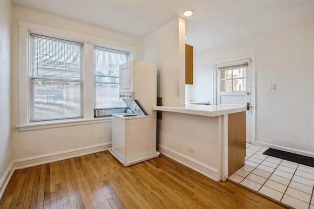 kitchen with stacked washer / drying machine, tile counters, kitchen peninsula, plenty of natural light, and light hardwood / wood-style flooring