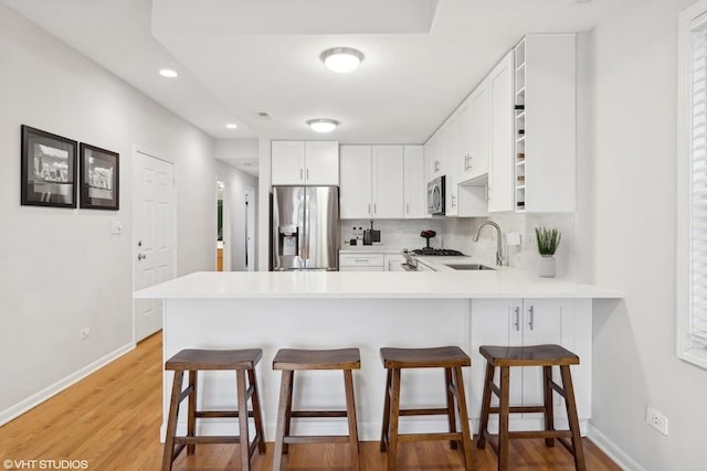 kitchen featuring white cabinetry, sink, backsplash, kitchen peninsula, and stainless steel appliances