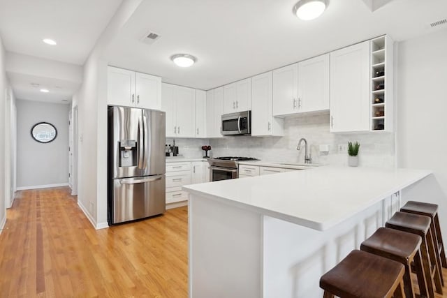 kitchen featuring white cabinetry, sink, a breakfast bar area, kitchen peninsula, and stainless steel appliances