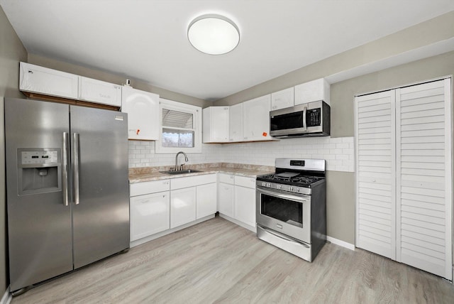 kitchen with appliances with stainless steel finishes, tasteful backsplash, white cabinetry, sink, and light hardwood / wood-style floors