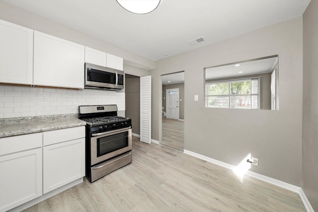 kitchen with tasteful backsplash, light stone counters, appliances with stainless steel finishes, light hardwood / wood-style floors, and white cabinets