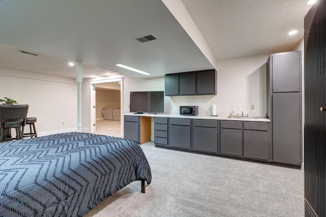 bedroom featuring connected bathroom, sink, fridge, light carpet, and a textured ceiling