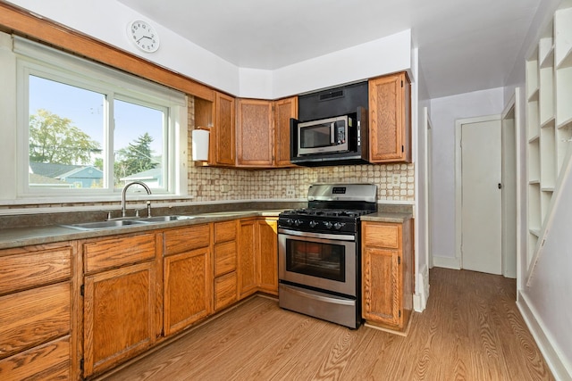 kitchen featuring stainless steel appliances, sink, decorative backsplash, and light wood-type flooring