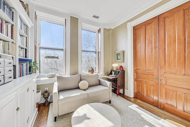 living area with crown molding, a healthy amount of sunlight, and light wood-type flooring